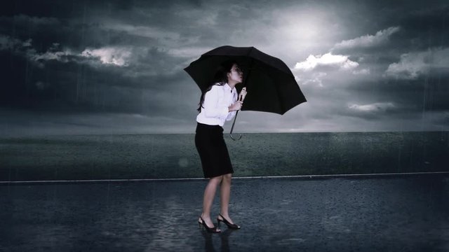 Video footage of a young worried businesswoman holds umbrella on rainy day, shot outdoors