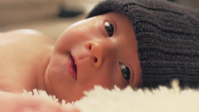 A charming little baby boy is looking into the camera and is wearing a black hat.
