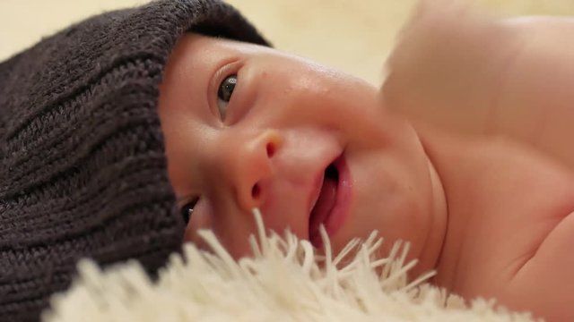 A charming little baby boy is looking into the camera and is wearing a black hat.