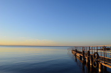Fototapeta premium The old pier in the Volga River, lit by the sun at sunset, surrounded by water and clear sky