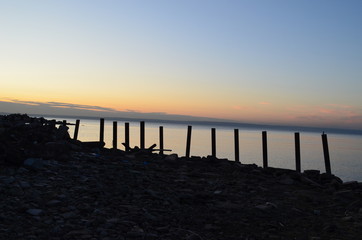 Obraz premium The old pier in the Volga River, lit by the sun at sunset, surrounded by water and clear sky