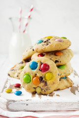 Stack of children's cookies with colorful chocolate candies in a sugar glaze on a white light wooden background. Selective focus