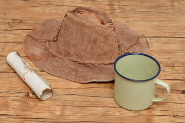 An old leather hat with a paper scroll and tin mug