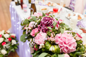 Decoration a bouquet of flowers of table of the newlyweds. Indoors wedding reception venue with festive decor. Tables for the newlyweds with flowers