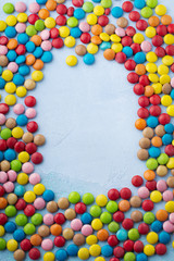 Chocolate round candy in a multicolored sugar glaze on light blue background. Selective focus. Top view. Place for text.