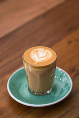 A Cup of Piccolo latte coffee with latte art and green saucer on the wooden table background.