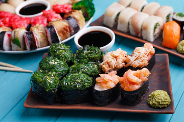 Sushi restaurant menu, Japanese food, delicious seafood concept. Great delicious set of colorful sushi rolls served on the plates with soy sauce and wasabi, tasty dinner for big company