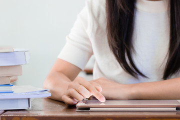 Fototapeta premium Close up on woman right hand using tablet next to pile of book on wooden table