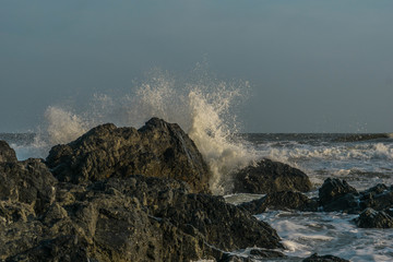 Fototapeta na wymiar Waves crashing over black rocks on the sea shore. Vung Tau, Vietnam.
