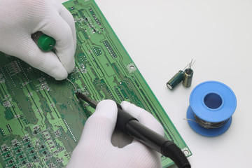A man in antistatic gloves holding a solder and a soldering iron repairs an electronic component on...