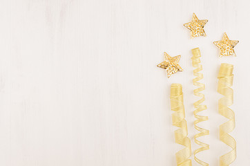 Christmas decorations, firework of gold stars and curl ribbon on white wooden background. Top view, copy space.