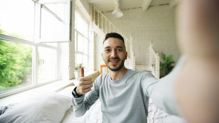 Young bearded man using tablet computer having video chat sitting in bed at home