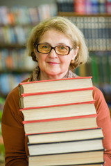 Happy senior woman with books in library