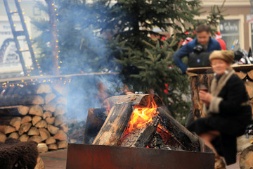 Kobieta grzeje się przy ognisku trzymając w dłoniach kubek z gorącym napojem. - obrazy, fototapety, plakaty