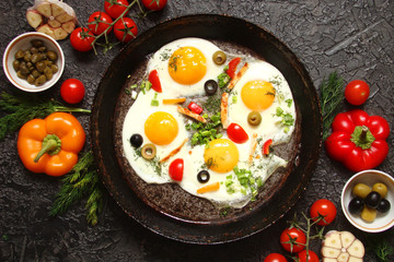 Fried eggs in a cast iron pan with peppers, tomatoes, capers, herbs and bread on a black background