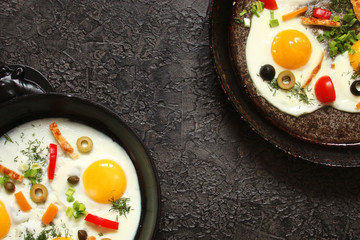 Fried eggs in a cast iron pan with peppers, tomatoes, capers, herbs and bread on a black background