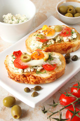 Bruschetta, crostini with cream cheese, with cherry tomatoes, herbs, olives, capers and fried egg