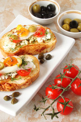 Bruschetta, crostini with cream cheese, with cherry tomatoes, herbs, olives, capers and fried egg