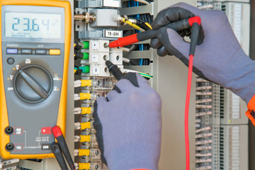 Electrician and instrument worker wearing safety gloves measuring voltage and checking electric circuit by using digital multi meter, maintenance and service job.