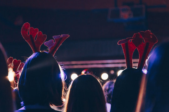 rear view of audience wearing christmas deer horns at a christmas concert. silhouettes of concert crowd in front of bright stage lights.