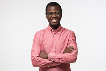 Portrait of smiling handsome african american business man in casual pink shirt standing with crossed arms isolated on gray background