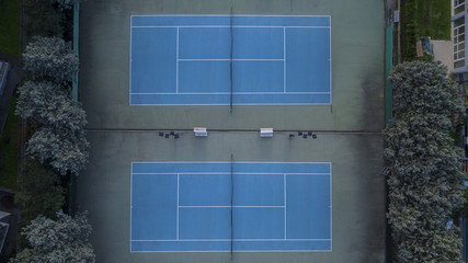 Vista aerea perpendicolare di un centro sportivo con campi da tennis in cemento. La pavimentazione del campo è blu mentre i bordi sono verdi. I campi da gioco sono vuoti.