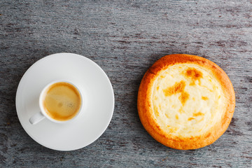 a cup of espresso on a plate and a bun on a wooden background