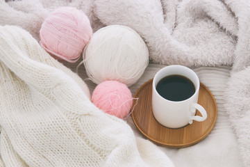 Obraz na płótnie Canvas Cup of coffee and woolen balls over cozy and white blanket. Top view.