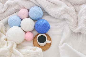 Fototapeta na wymiar Cup of coffee and woolen balls over cozy and white blanket. Top view.