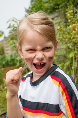 Kind mit Deutschland Flagge auf der Wange und im Deutschland Trikot ballt die Faust und jubelt - obrazy, fototapety, plakaty