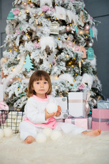 Emotional smiling little girl sitting in pajama with Christmas gifts near New Year's tree and playing snowballs