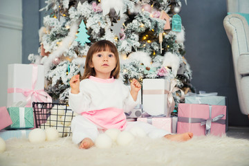 Emotional smiling little girl sitting in pajama with Christmas gifts near New Year's tree and playing snowballs