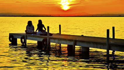 Naklejka na ściany i meble dos amigas drisfrutando de la puesta de sol en el lago
