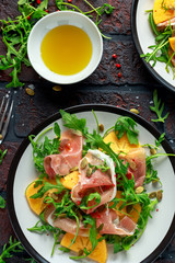 Fresh Tasty Persimmon salad with arugula, parma ham, olive oil, pumpkin seeds and herbs. autumn, winter healthy food