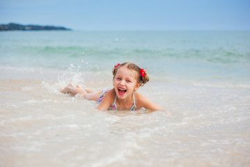 Fototapeta na wymiar Happy girl with two pigtails floats lying on the sand by the sea, and enjoys playing