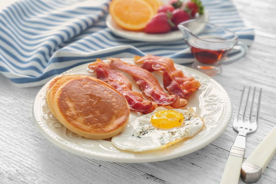 Plate with yummy pancakes, fried bacon and egg on wooden table