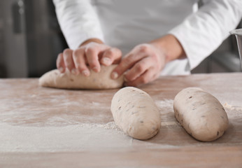 Raw loaves of bread on table and man in bakery