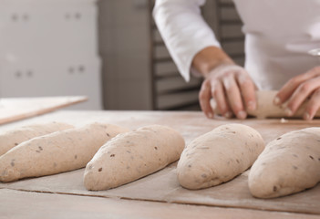 Raw loaves of bread on table and man in bakery