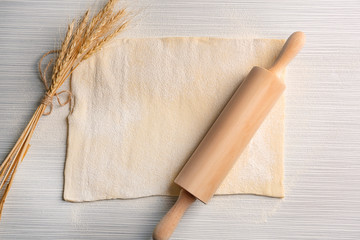 Raw puff dough, rolling pin and wheat spikes on table