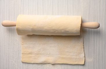 Raw puff dough and rolling pin on table