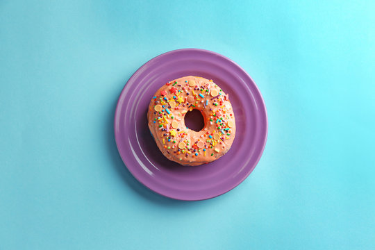 Plate with tasty donut on color background