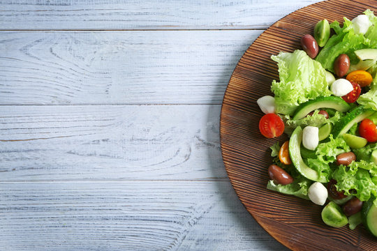 Board with delicious vegetable salad on wooden background
