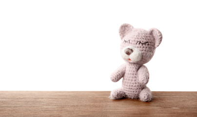 Cute knitted toy bear on table against white background