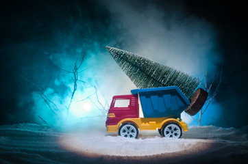 Miniature car with fir tree on Snowy Winter Fores, or toy car carrying a christmas tree and at night time