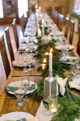 holidays, interior, amusement concept. adorable christmas decor of the long table in restaurant, created by candles in hamdmade holders of silver colour and branches of some fur tree