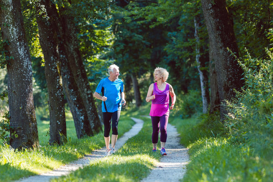 Full length front view of two active seniors with a healthy lifestyle smiling while jogging together outdoors in the park