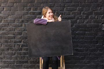 emotions, art, advertisment concept. extremely woman with shining smile is keeping on her knees not big blackboard with free space for text, she is giving a thumb up
