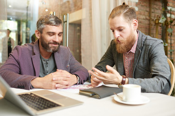Portrait of two successful business men discussing work and using laptop during meeting in cafe on coffee break