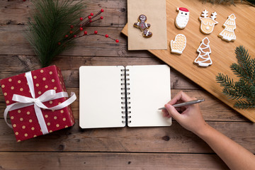 Female hands writing in open notebook with gift box and tasty christmas homemade cookies.