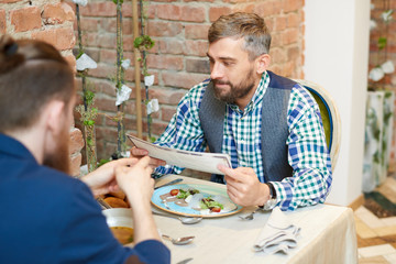 Portrait of mature bearded man reading menu while enjoying meal in modern cafe during lunch break